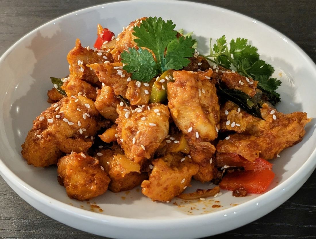 A plate of Kolkata-style chili chicken garnished with sesame seeds and cilantro, cooked by Utsav & Adda