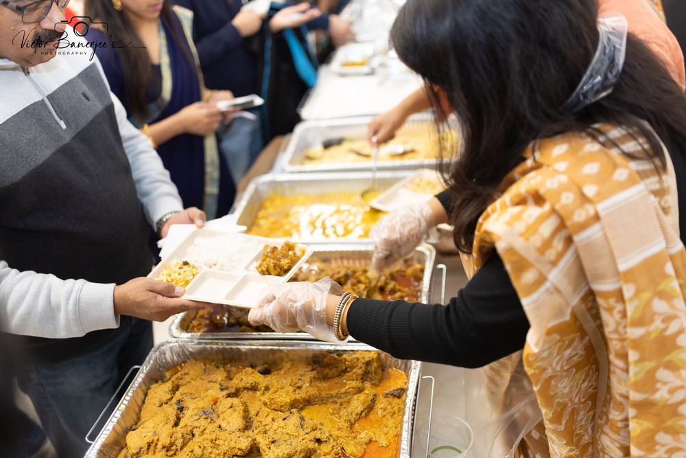 Volunteers serving food to guests along a buffet line at an Utsav & Adda festival food court